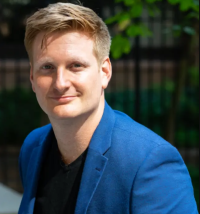 A smiling man with blond hair wearing a blue jacket